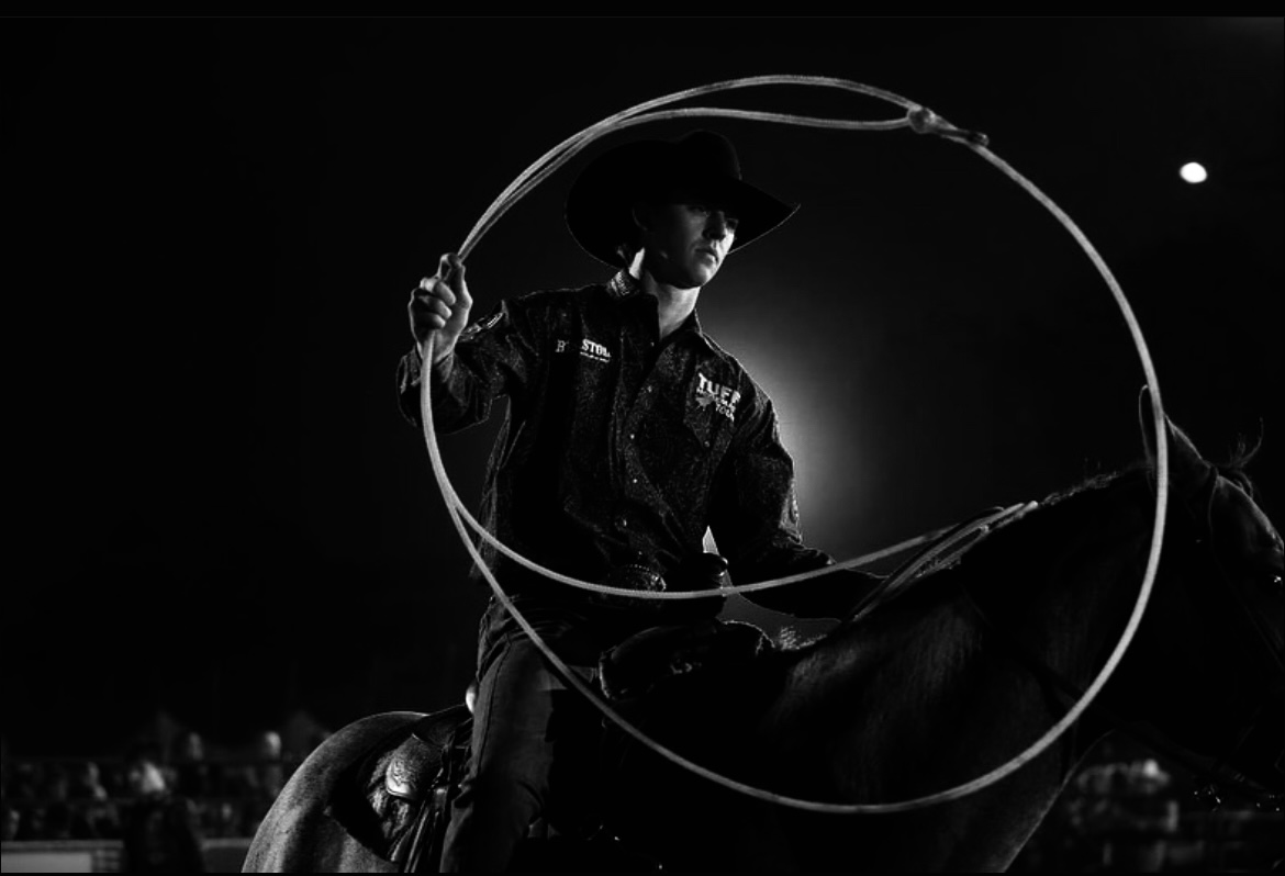 Rodeo athlete swinging a rope beneath dramatic arena lighting